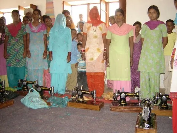Village women standing behind a row of sewing machines at a tailoring center
