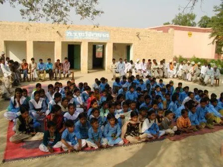 Students in blue uniforms sitting outside a village school near Raisingh Nagar